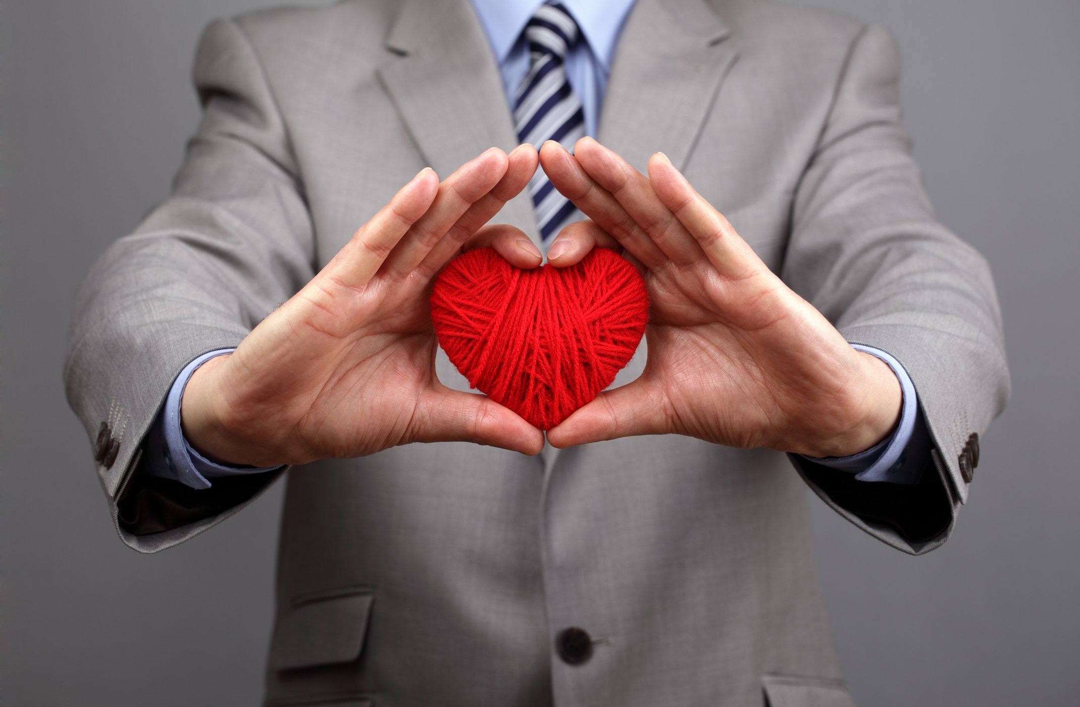 A person in a business suit holding out yarn in the shape of a heart. 