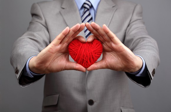 A person in a business suit holding out yarn in the shape of a heart. 