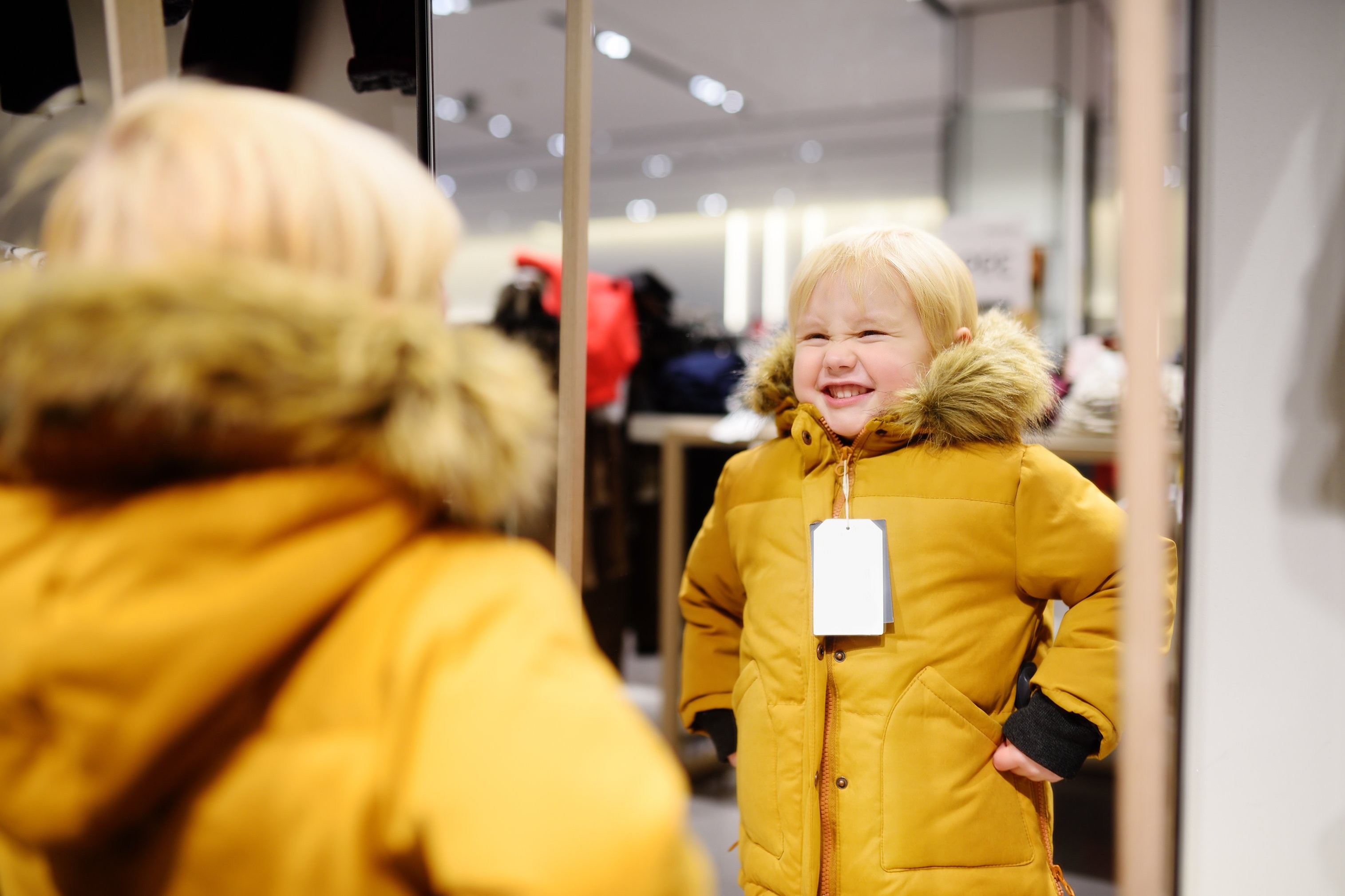A child trying on a coat and looking in the mirror