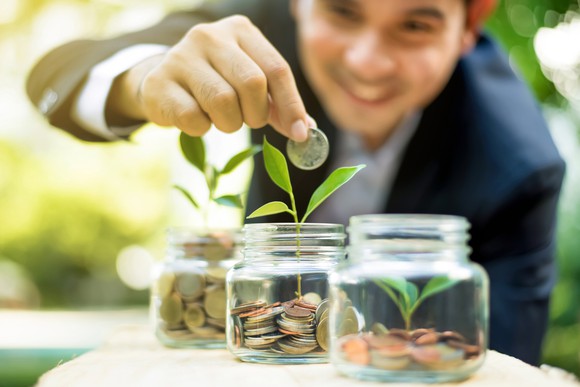 A man adds a coin to glass jars filled with coins and seedlings.