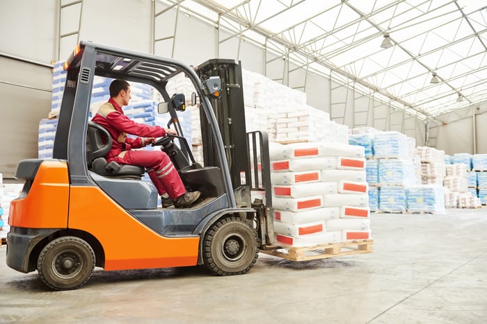 A forklift moves a loaded pallet in a warehouse.