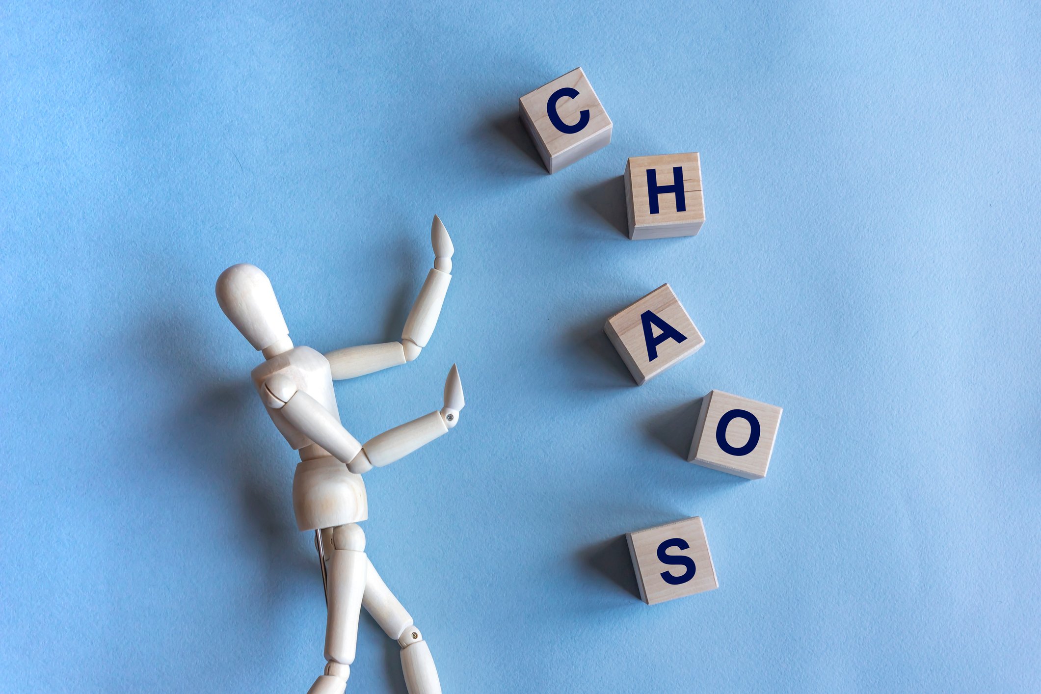 Chaos written in wooden cubes and a wooden mannequin on blue background. 