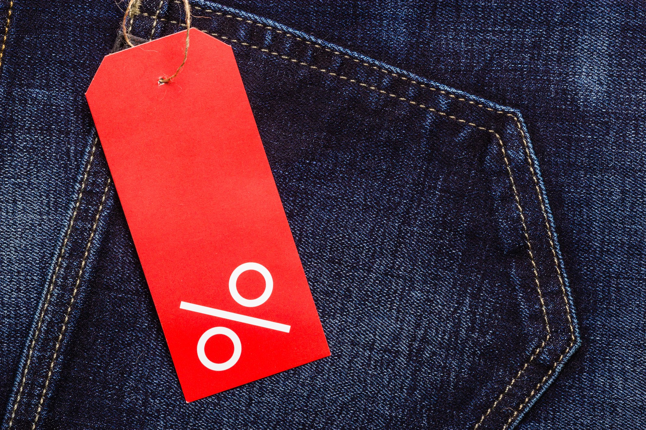 A pair of blue jeans with a red tag featuring a percent sign.