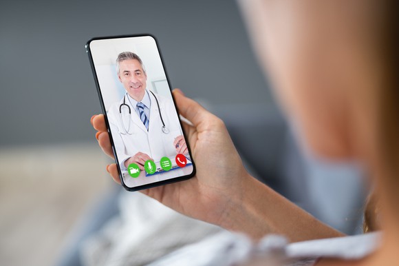 A person holds a smart phone, taking a video call from a doctor.