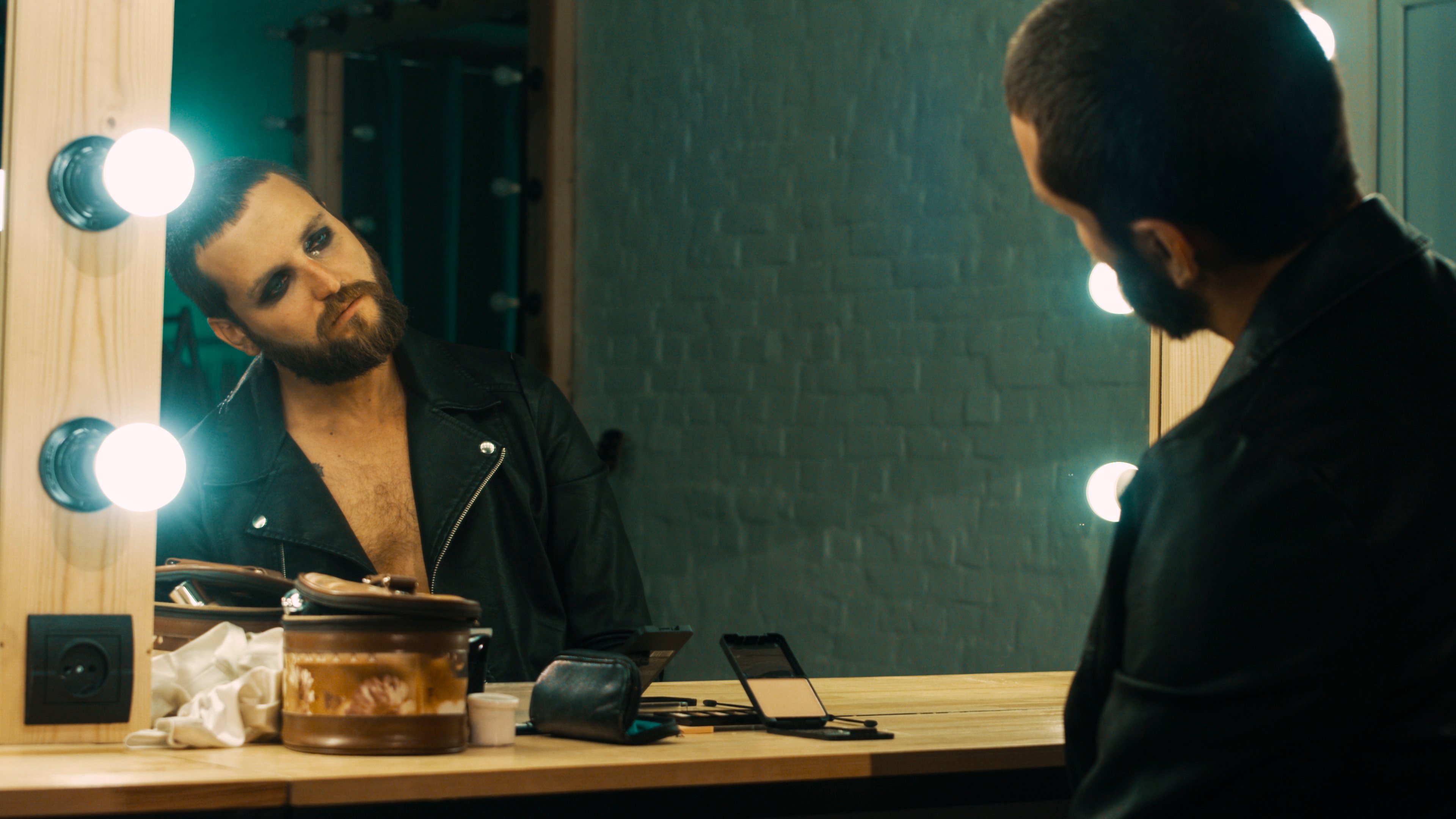 A tired rock star stares at himself in a large mirror.