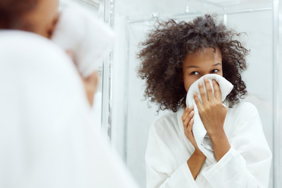 A woman looks in the mirror while she dries her face.