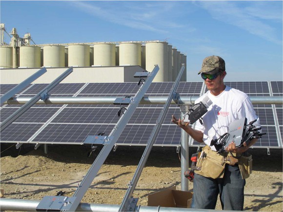 Installer next to framework for solar panels, holding an Enphase micro-inverter.
