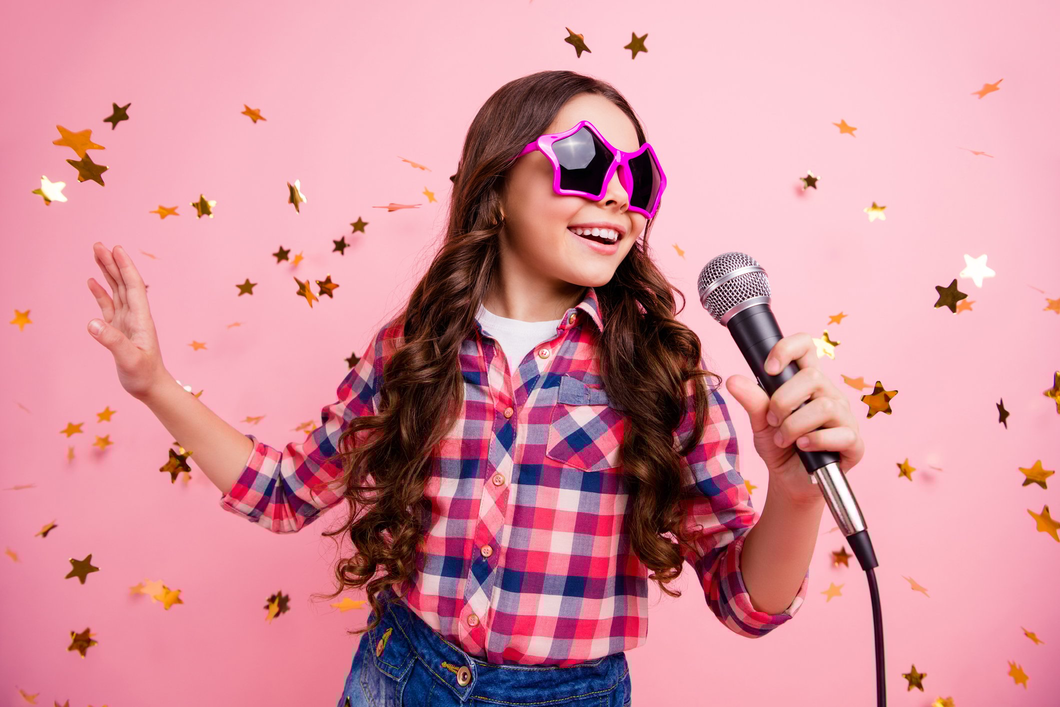 A young girl in star-shaped sunglasses sings a song.