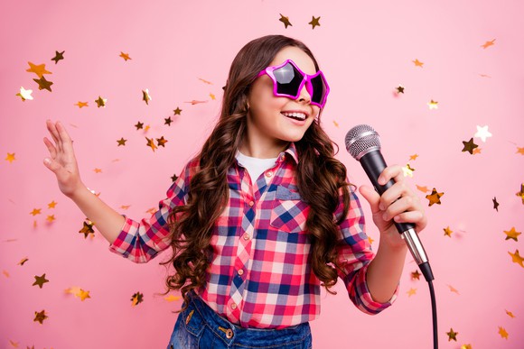 A young girl in star-shaped sunglasses sings a song.
