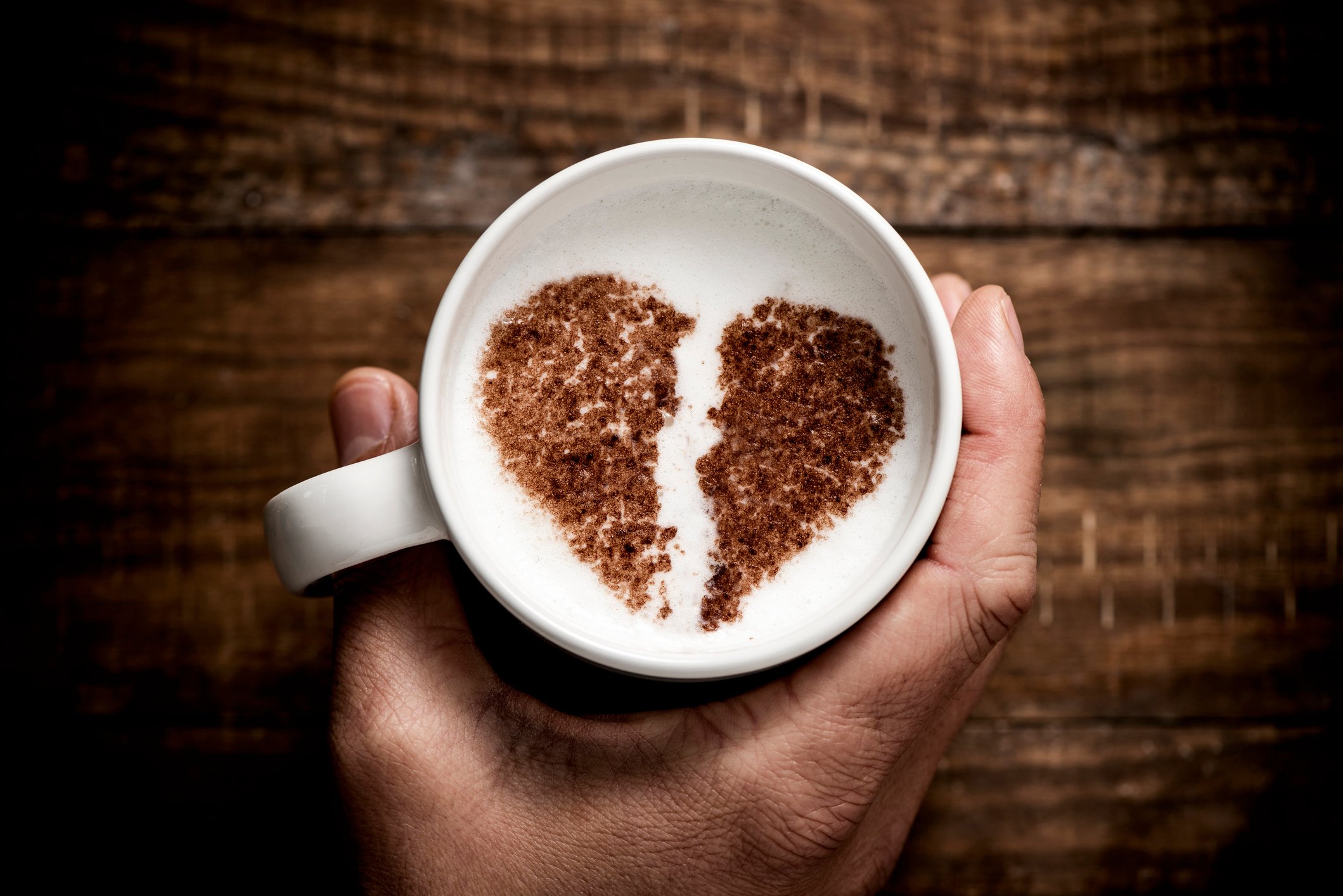 a white ceramic cup of cappuccino, with a broken heart drawn with cocoa powder on its milk foam