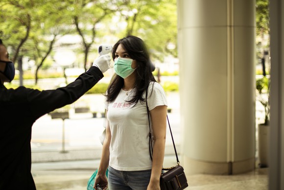 A woman outside a store getting her temp checked. 