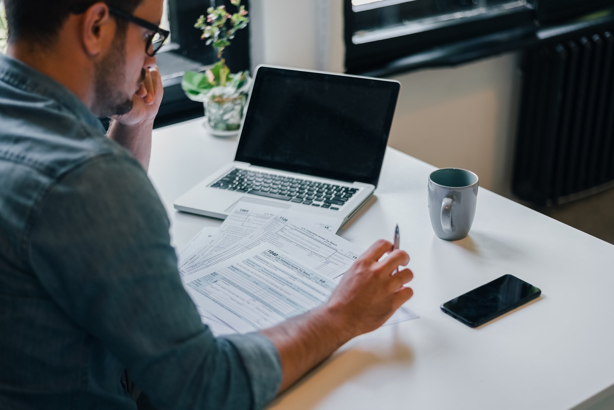 Man sitting at desk with laptop and tax forms.