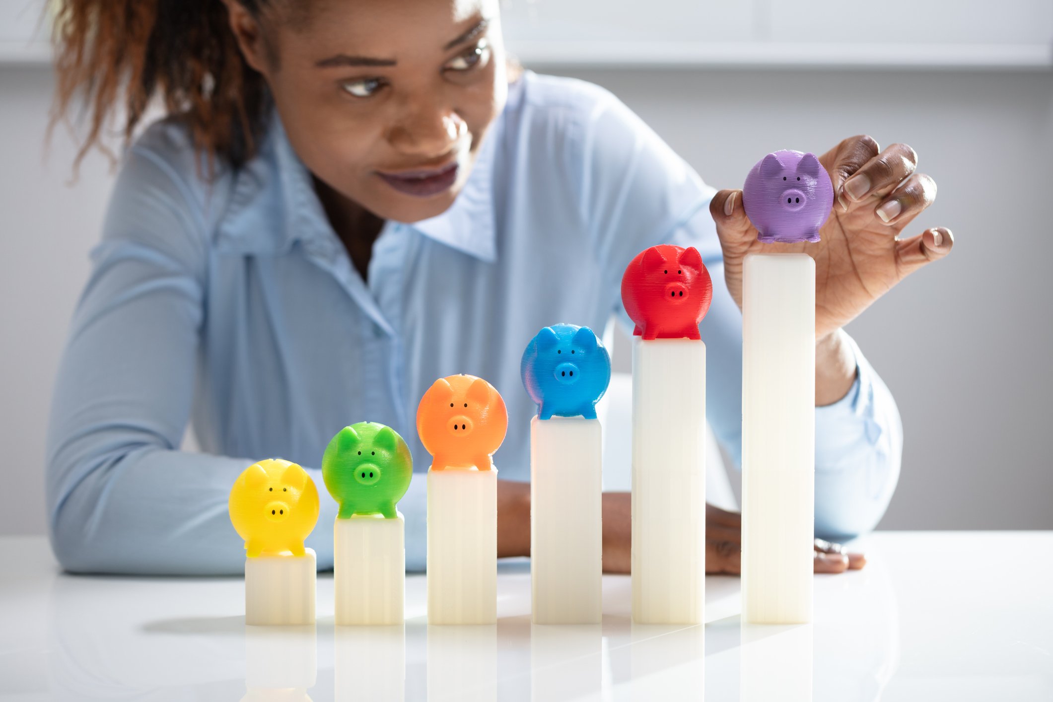 Woman stacking colored piggy banks on growing graph.