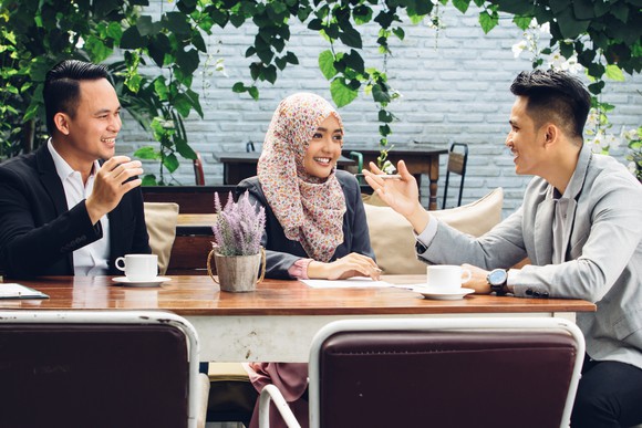 A woman and two men smiling and talking around a table