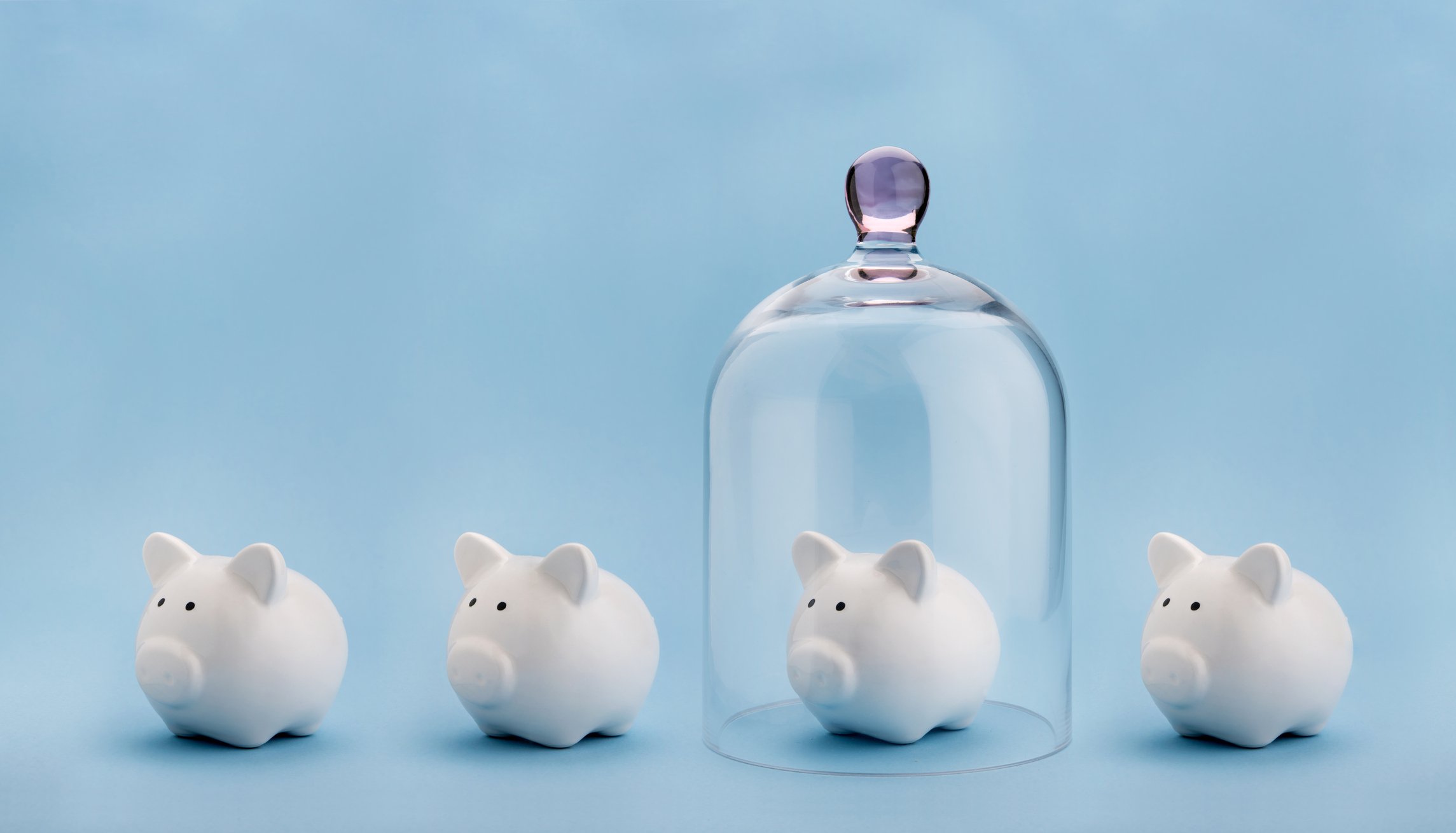three piggy banks with one covered by a clear upside-down glass jar protecting it.  