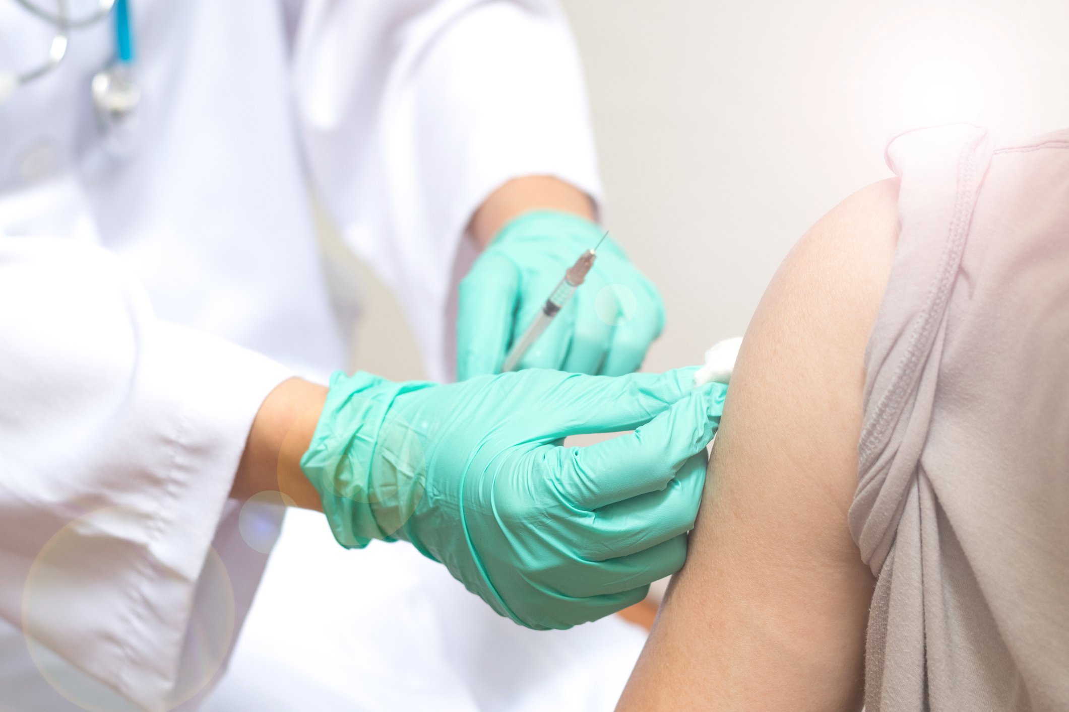 Healthcare professional holding cotton swab on a patient's arm and holding a syringe