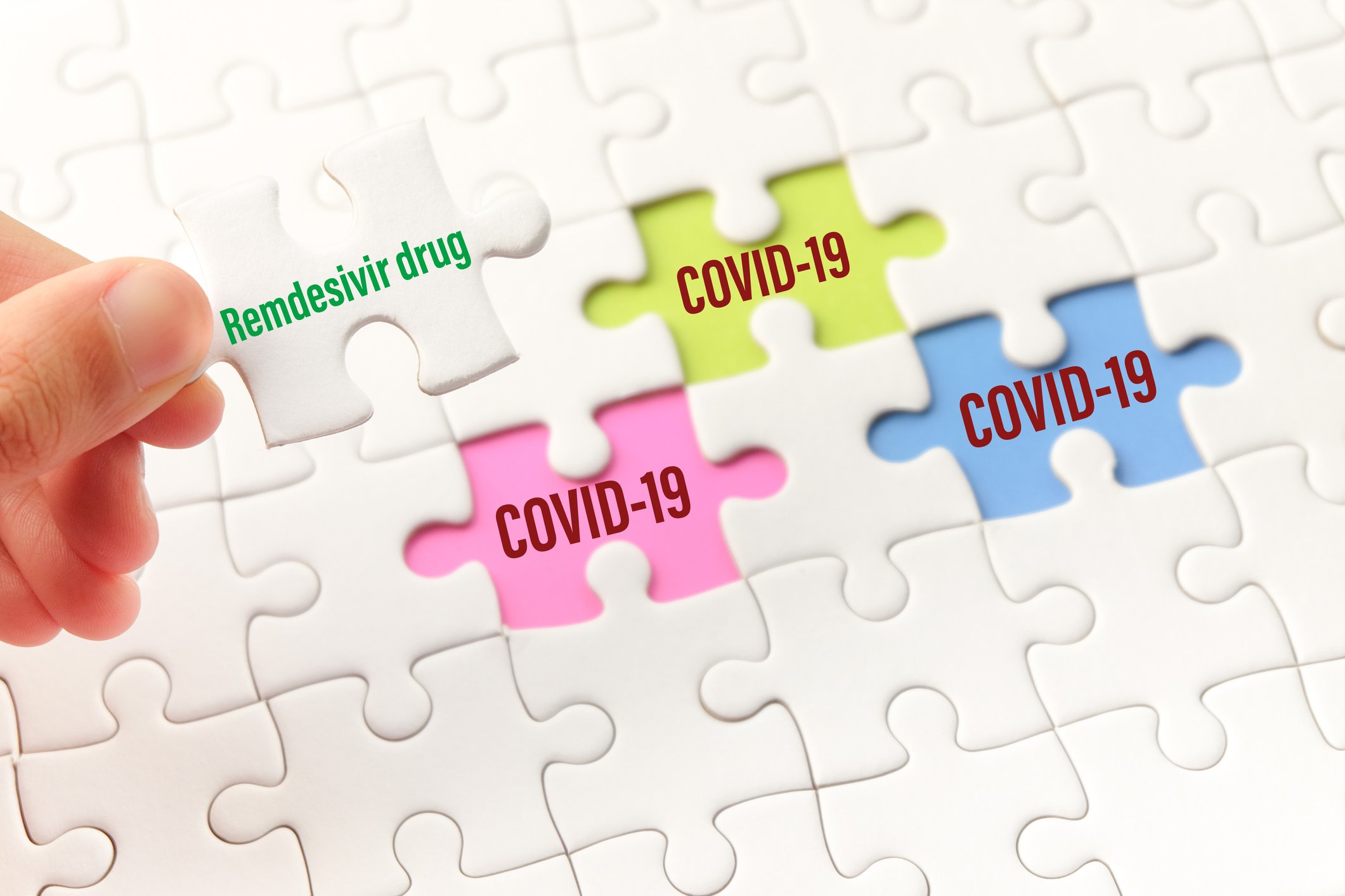 Jigsaw puzzle with "remdesivir drug" printed on one piece and COVID-19 printed on three empty spots