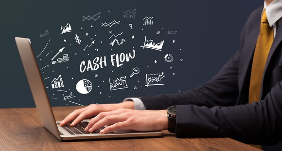 Someone sitting at a laptop in a suit and tie with various charts appearing to come out. The words Cash Flow are in the center.