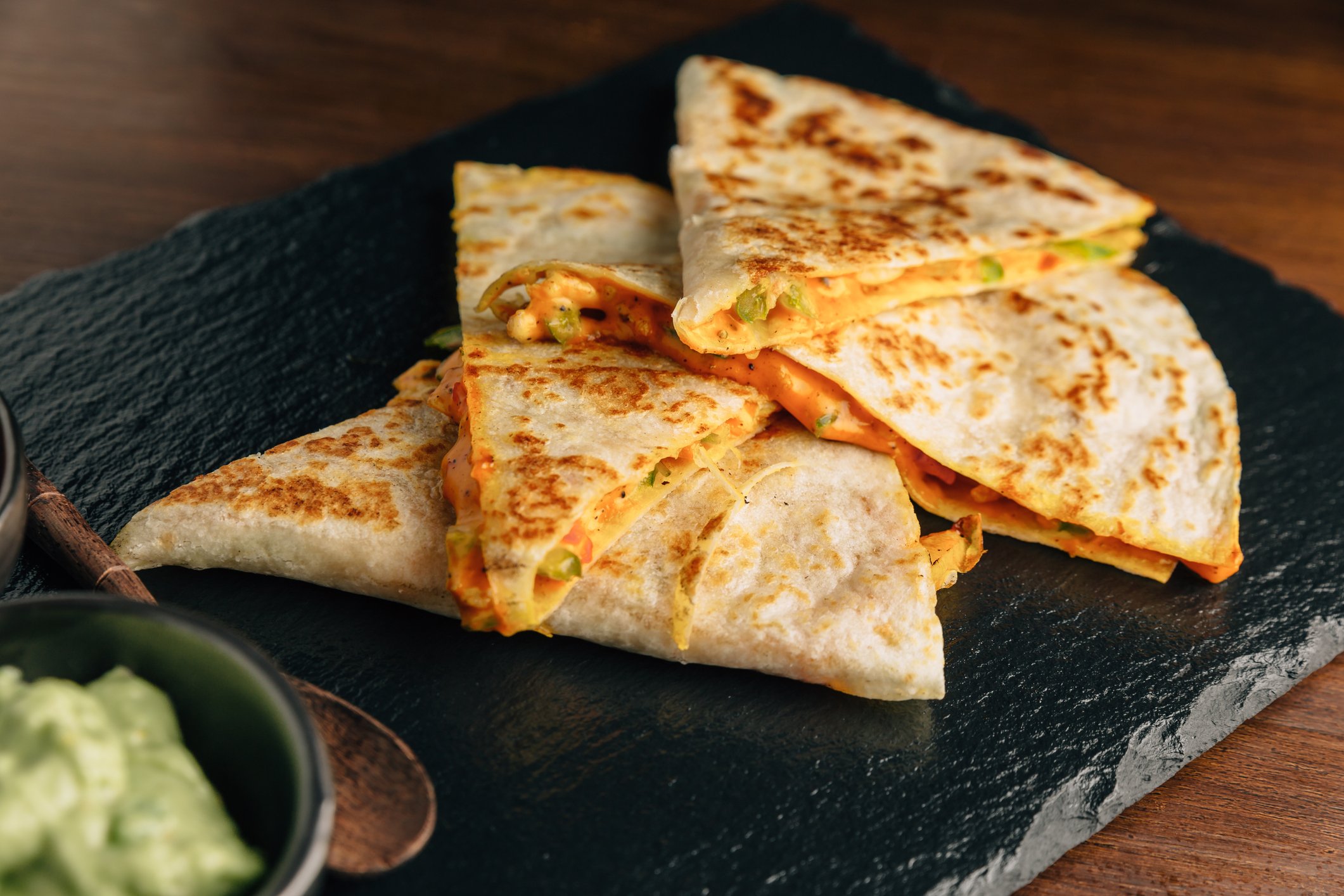  Chicken quesadilla slices served on a black wooden board.
