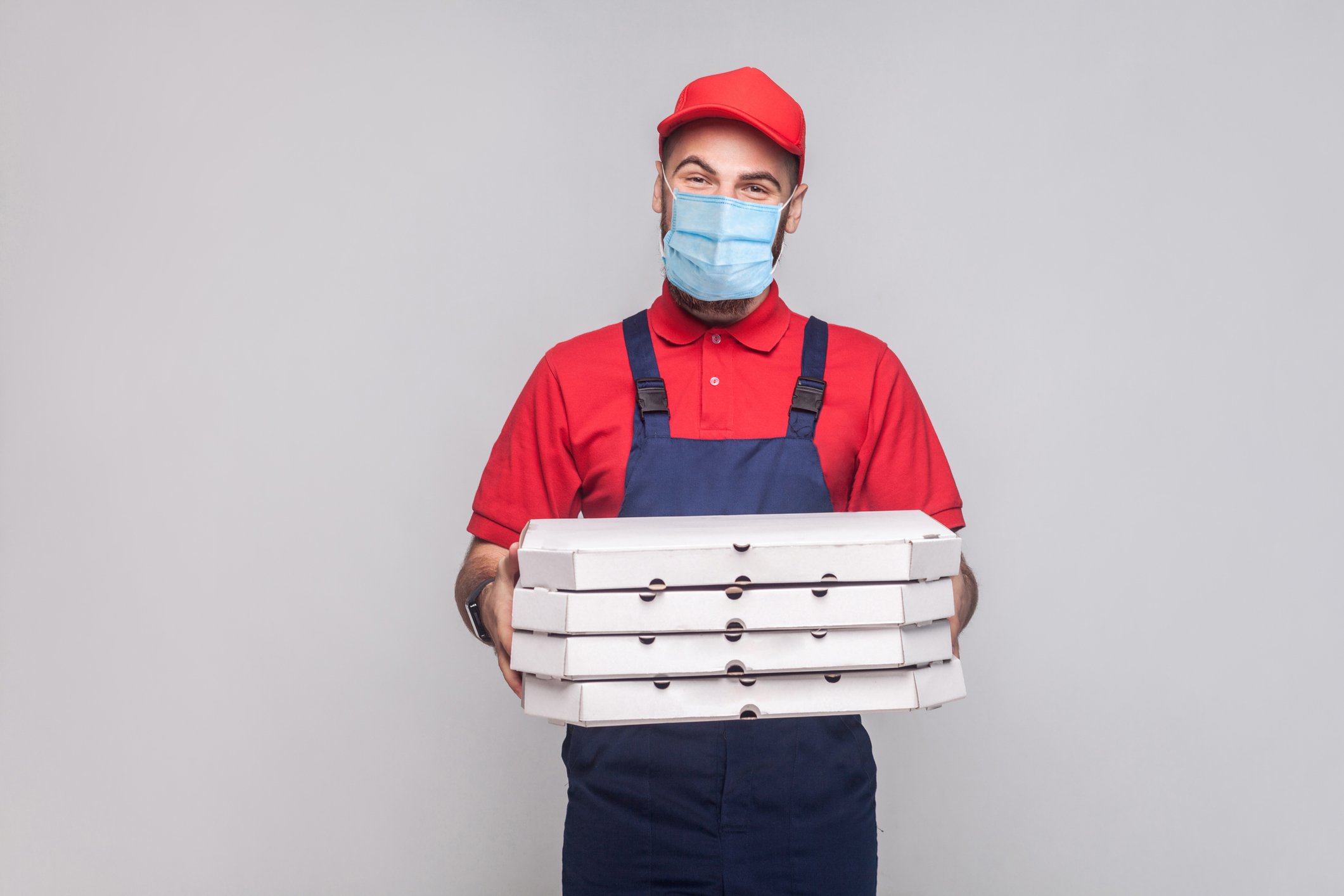 A man wearing a mask as he holds pizza delivery boxes.