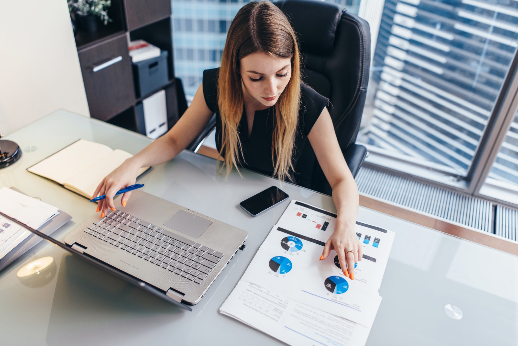 Young woman at her desk analyzing pie charts with her laptop.
