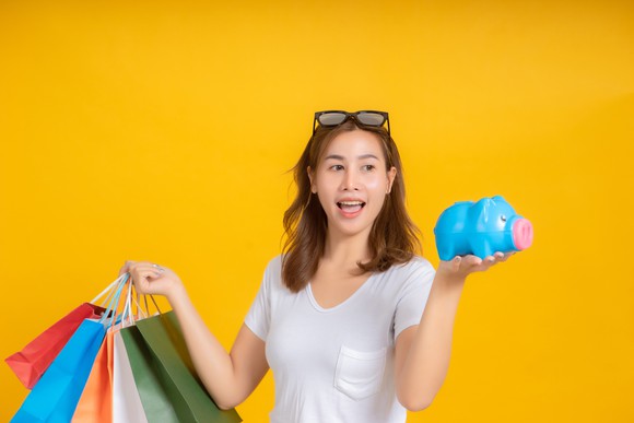 A woman with shopping bags in her right hand and a piggy bank in her left hand.