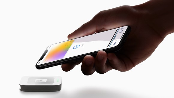 A hand holding an iPhone paying with the Apple card using Apple Pay.