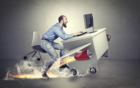 An office worker hangs on to his desk as it takes off on wings and jet-powered rockets