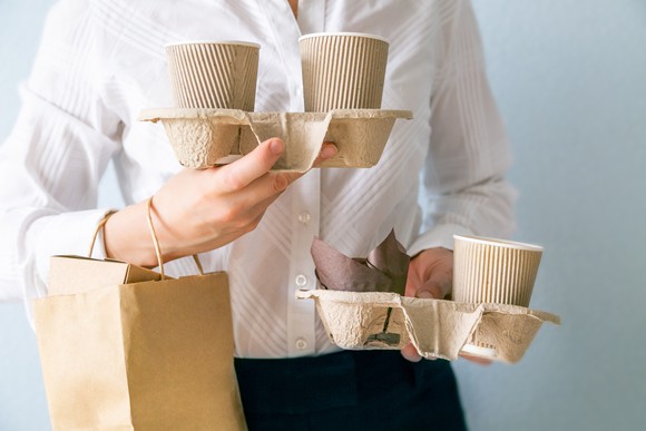 A person carries several coffee cups and a takeout bag.