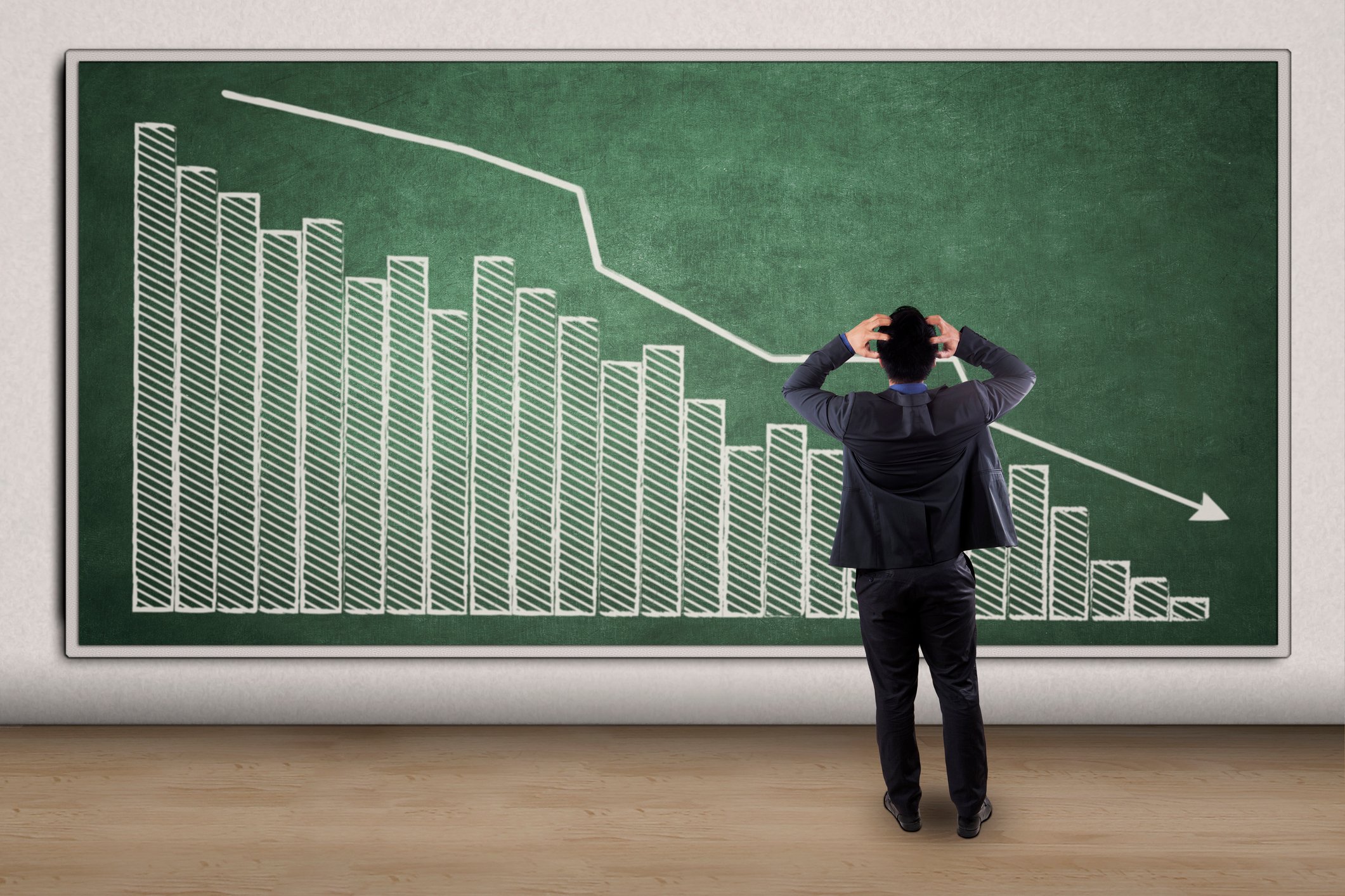 Man holding his head in panic, standing in front of a board with a downward pointing graph.