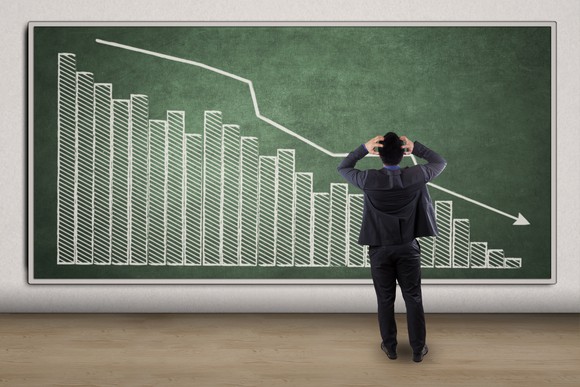 Man holding his head in panic, standing in front of a board with a downward pointing graph.