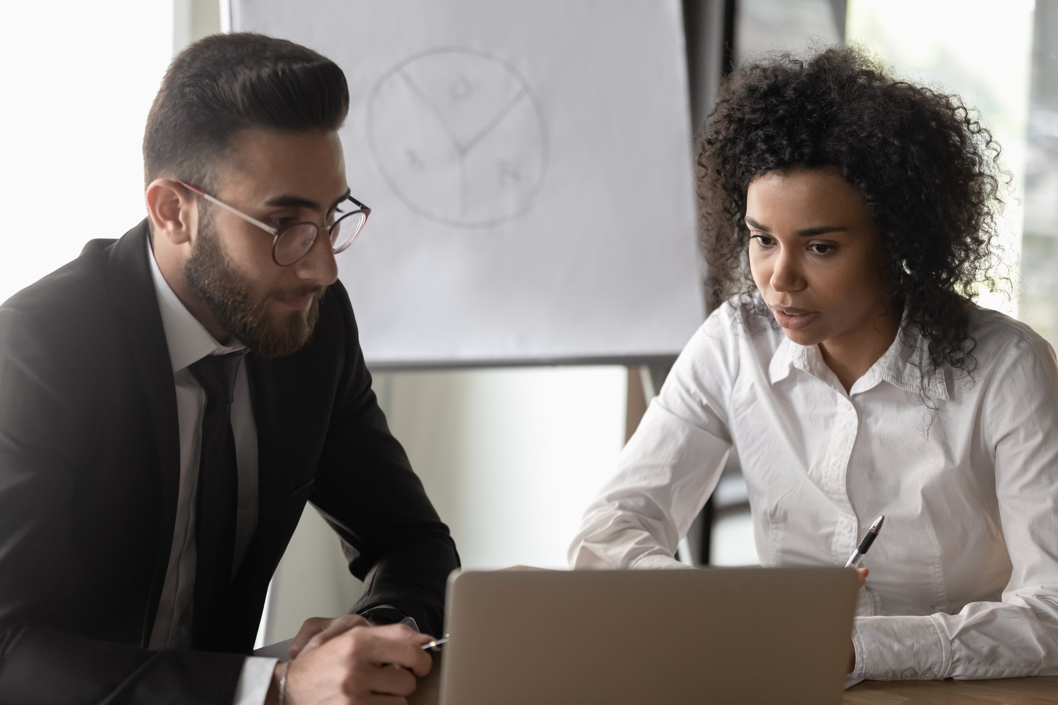 Businessman and businesswoman glancing at a screen to consider a decision.