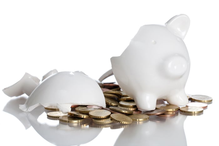 Broken white piggy bank with coins spilling out.