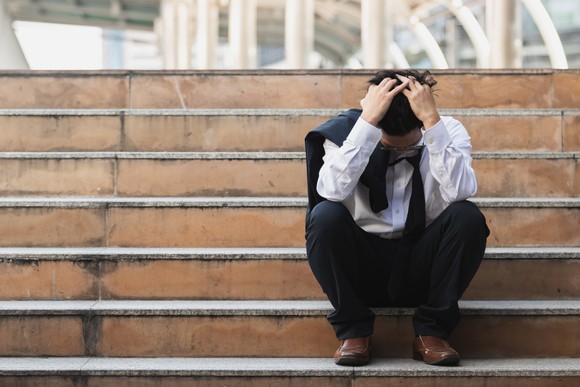 Frustrated young businessman holds his head  in his hands on the steps of an  office building. 