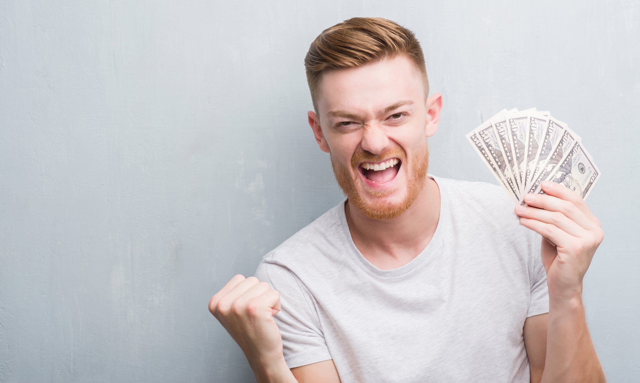 Man smiling while holding a fan of fifty dollar bills.