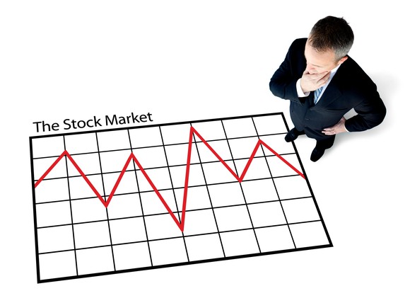 Man standing over large chart showing turbulent stock market trend.