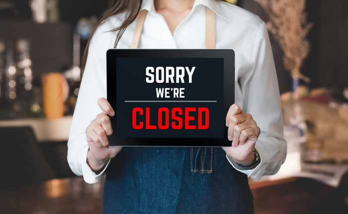 A store worker holds a sign reading Sorry we're closed.