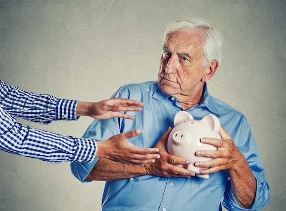 Older man holding piggy bank close to his chest, away from a pair of hands reaching to take the bank.