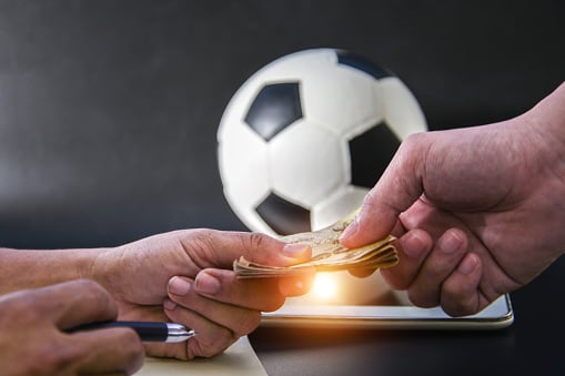 Two hands exchanging money in front of soccer ball