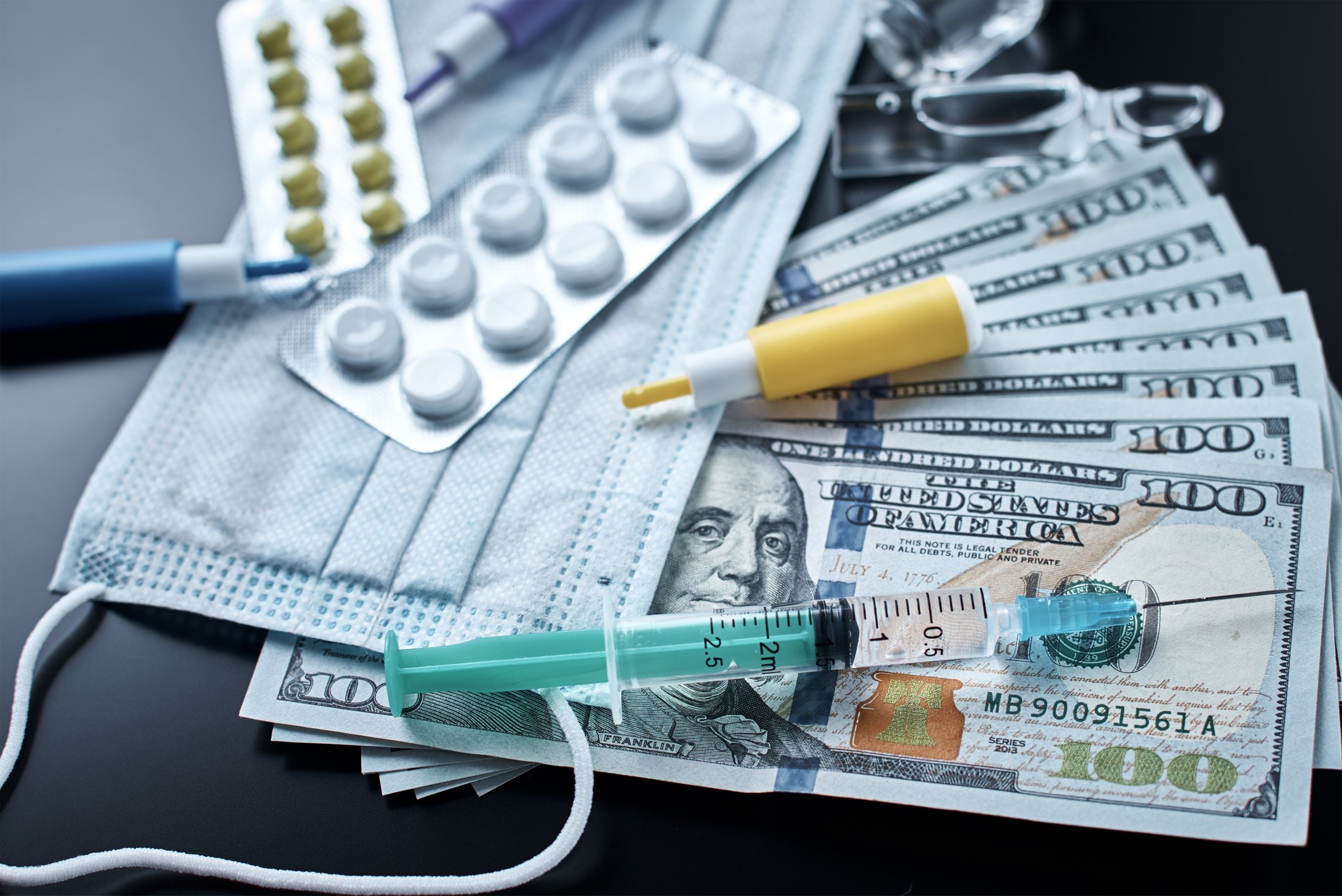Several pills and a syringe lying on top of several hundred-dollar bills.