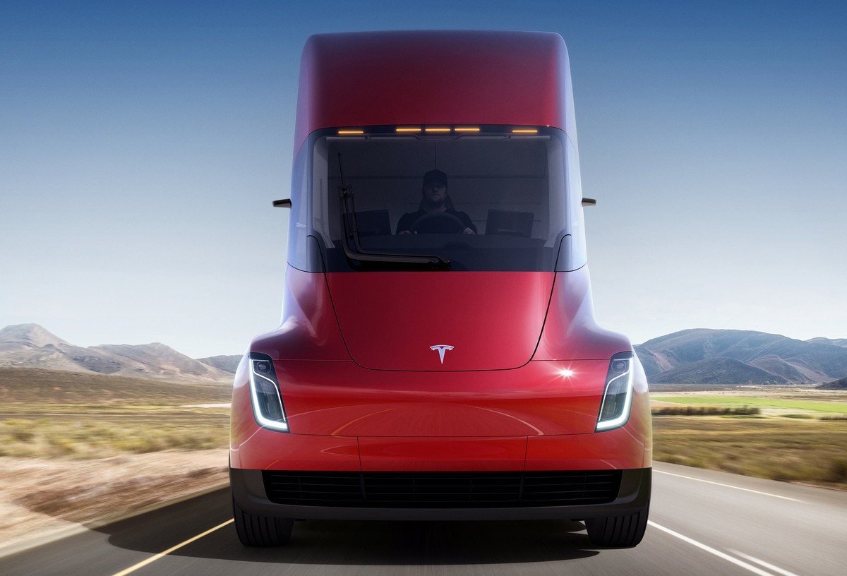 Red Tesla Semi as seen from front, on a road in semi-arid landscape.