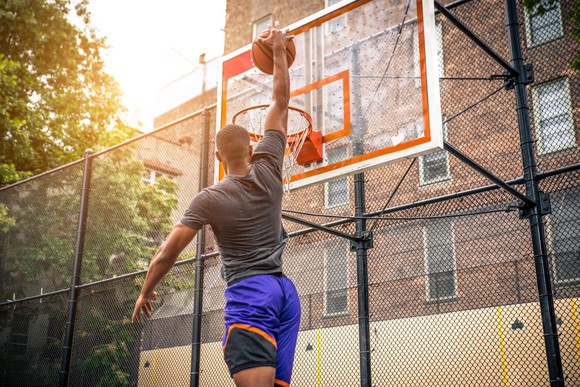 A basketball player makes a slam dunk at an outdoor court.