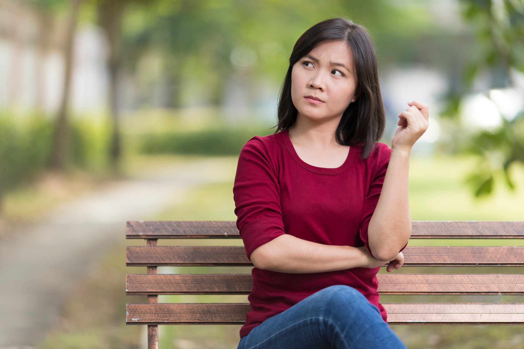 A woman sitting on park bench with a puzzled facial expression. 