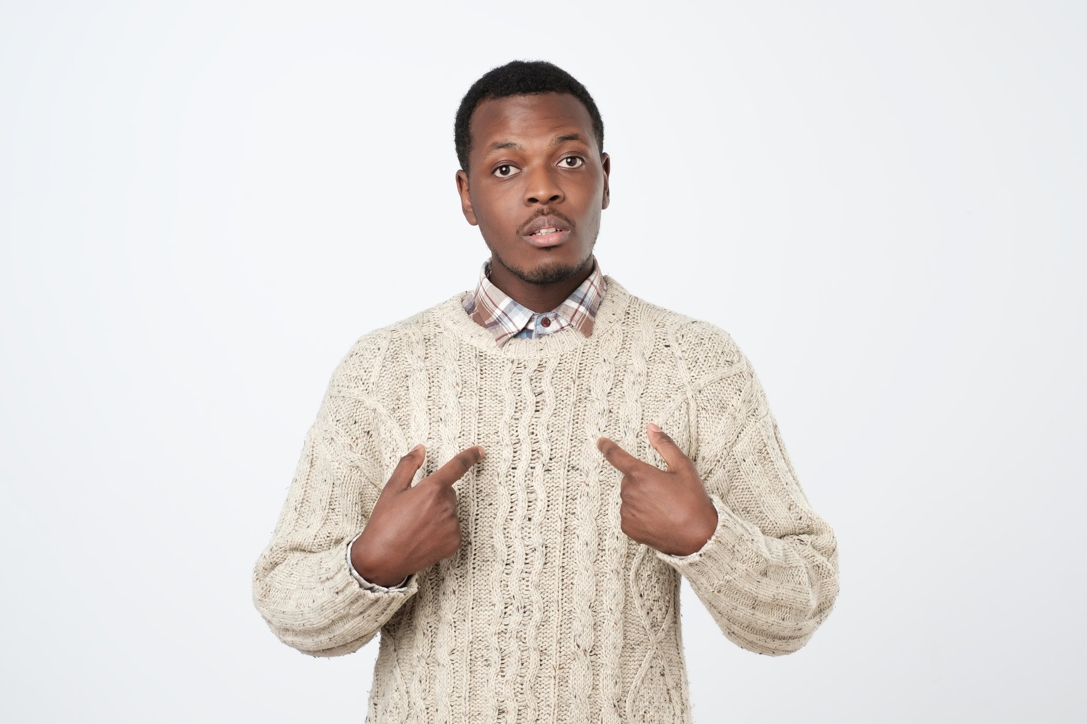 A young man is pointing to himself, surprised.