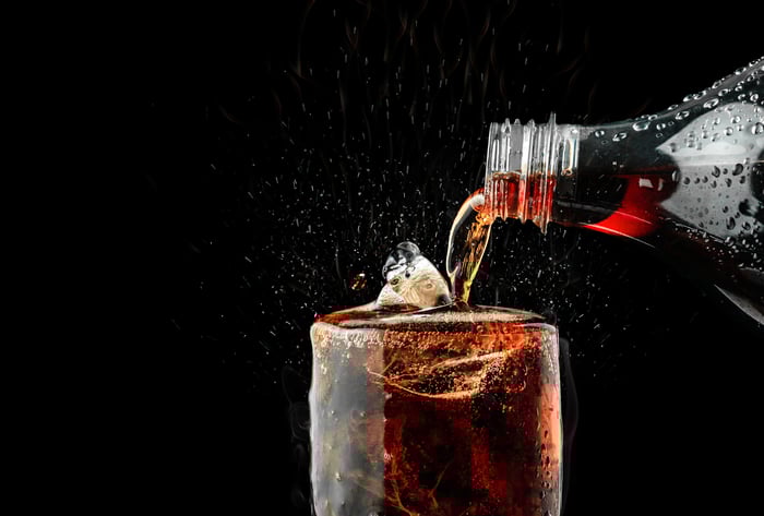 A soft drink is poured into a glass against a black background.