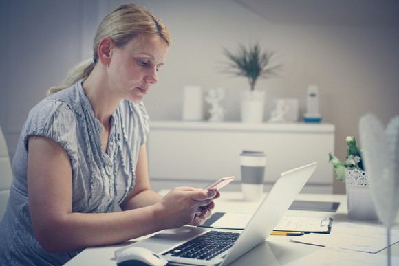 Worried woman looking at her phone in home office.