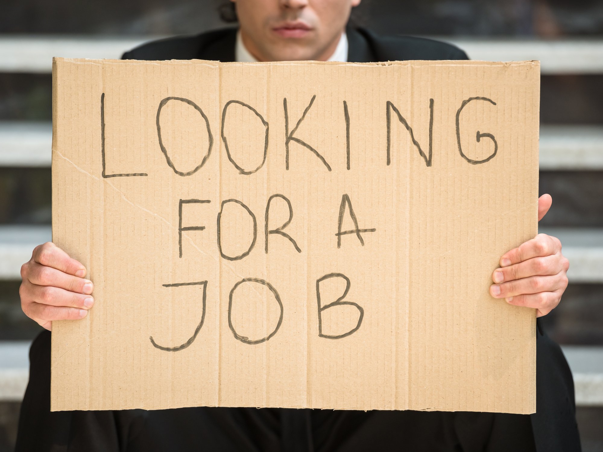 A businessman holding a cardboard sign that reads, Looking for a job. 