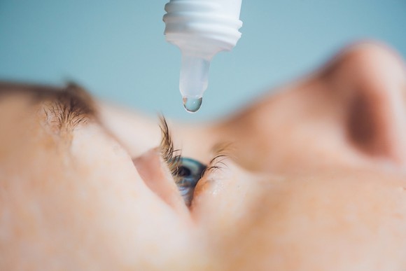 A person administering an eye drop.