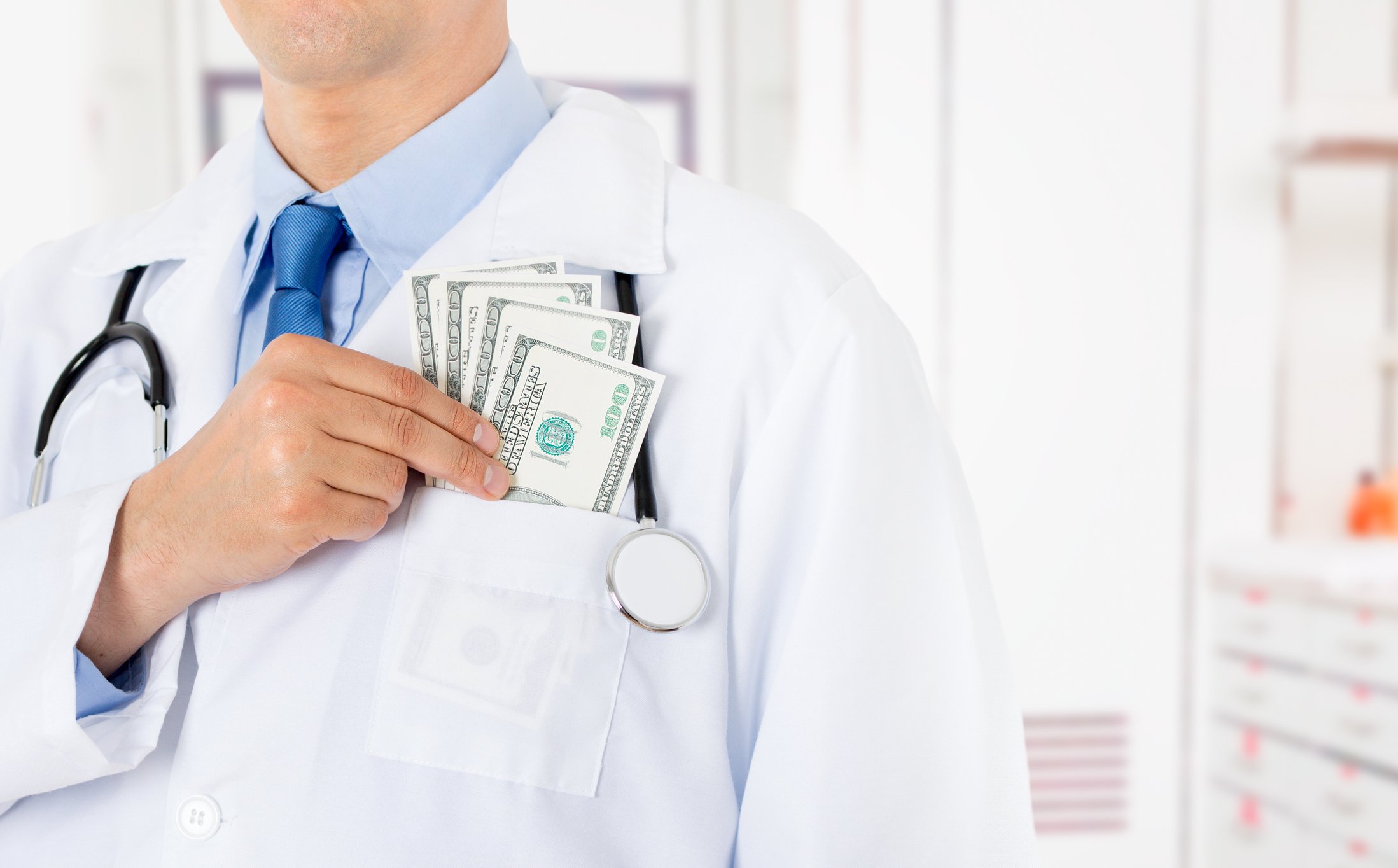 Male doctor putting $100 bills in his coat's front pocket