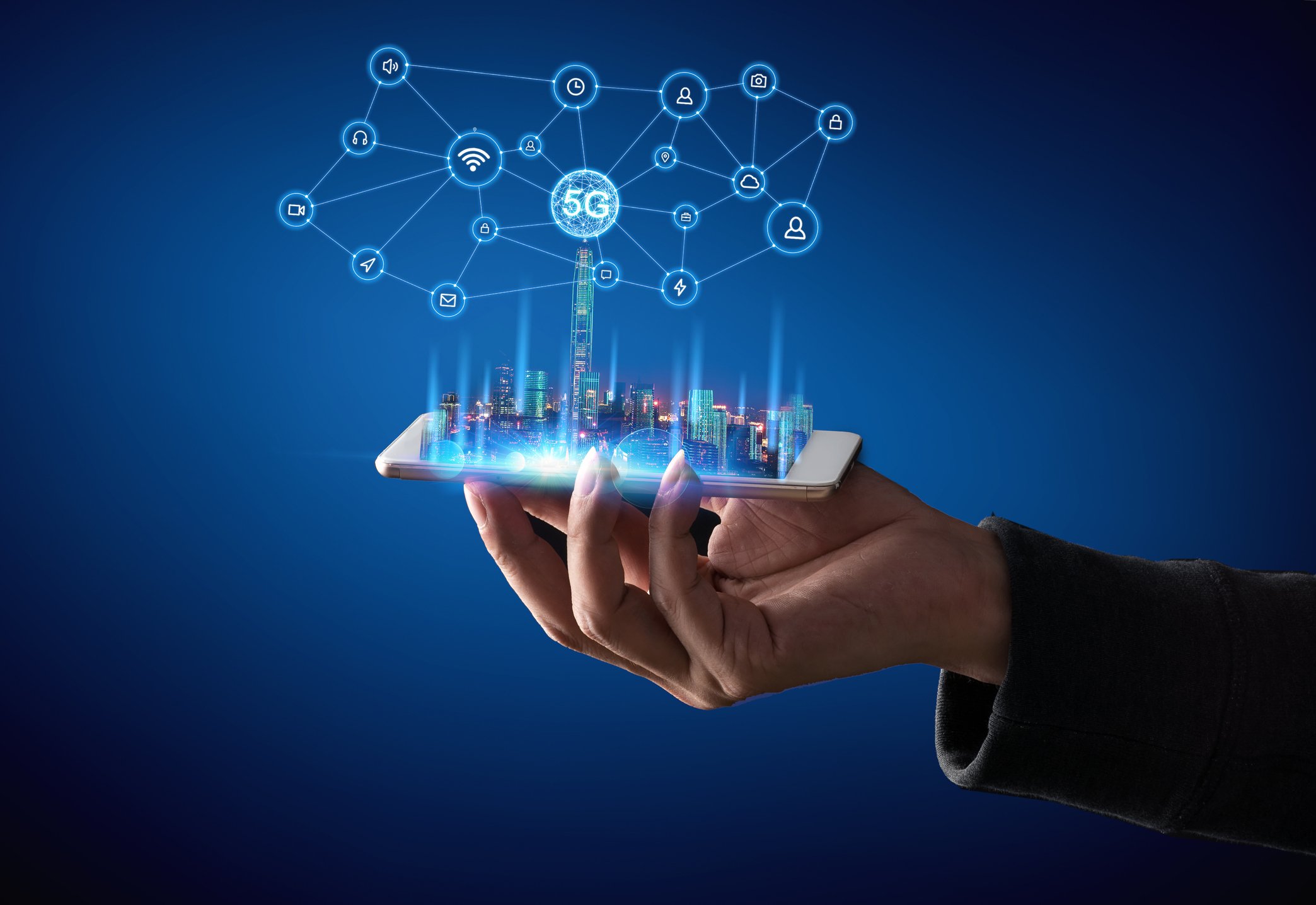 A hand holds a smartphone facing up and a 5G icon emerges upwards from the phone screen. 